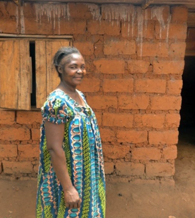 Jeannette stands proudly in front of her home that she built with the money saved from selling her farm's outputs.