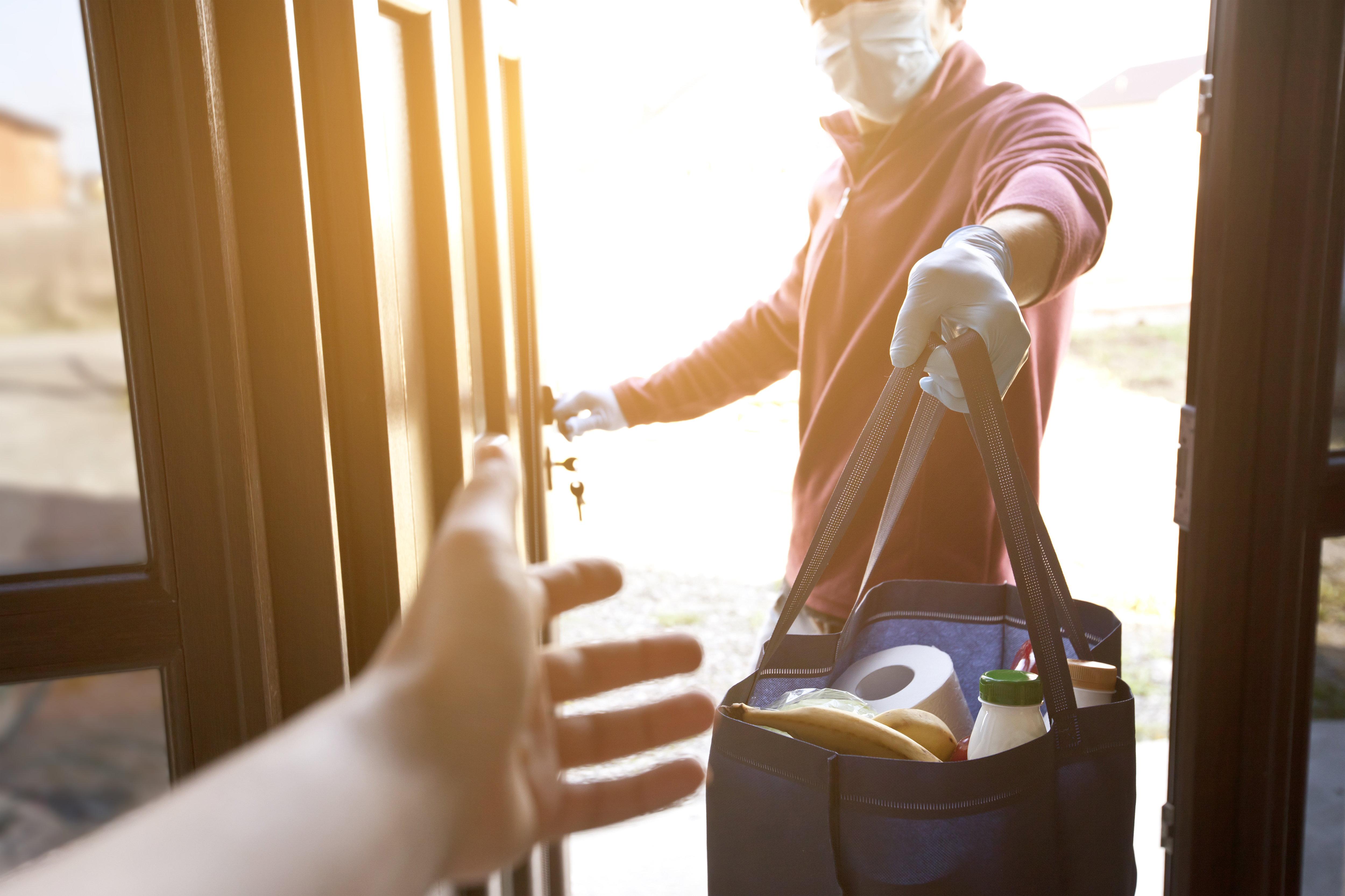 a man hands food shopping to a coronavirus-vulnerable person in their house