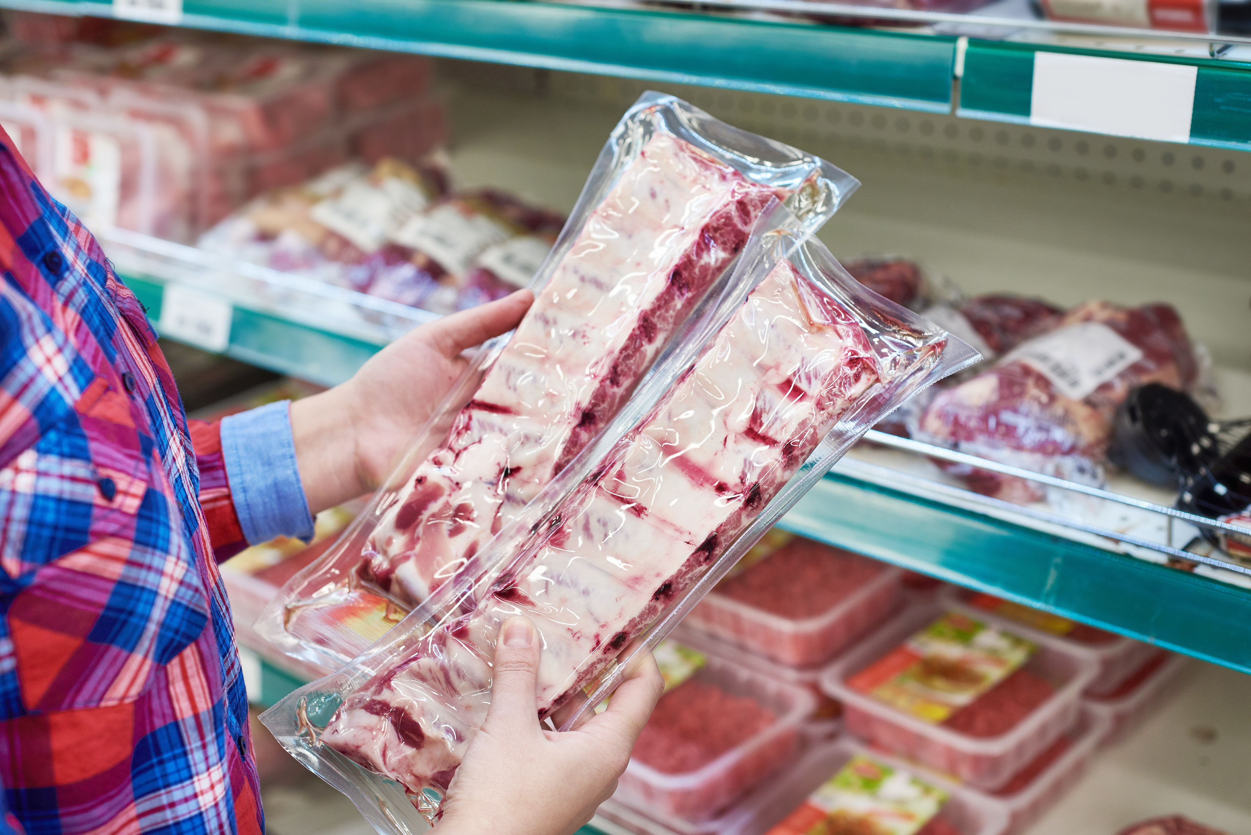 Man holding two packages of pork ribs in front of a grocery aisle