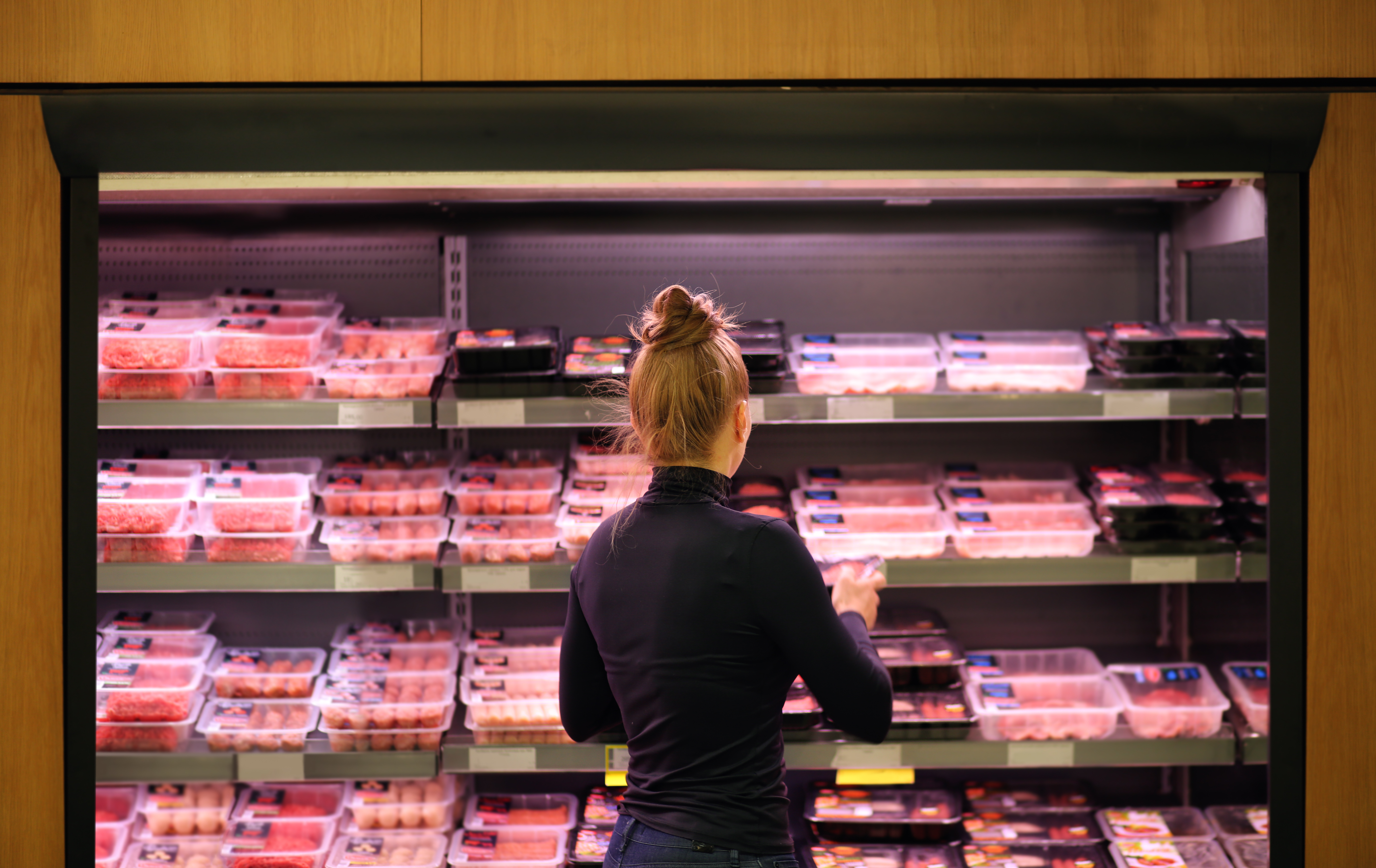 Woman with a shopping cart standing in front of a grocery meat case
