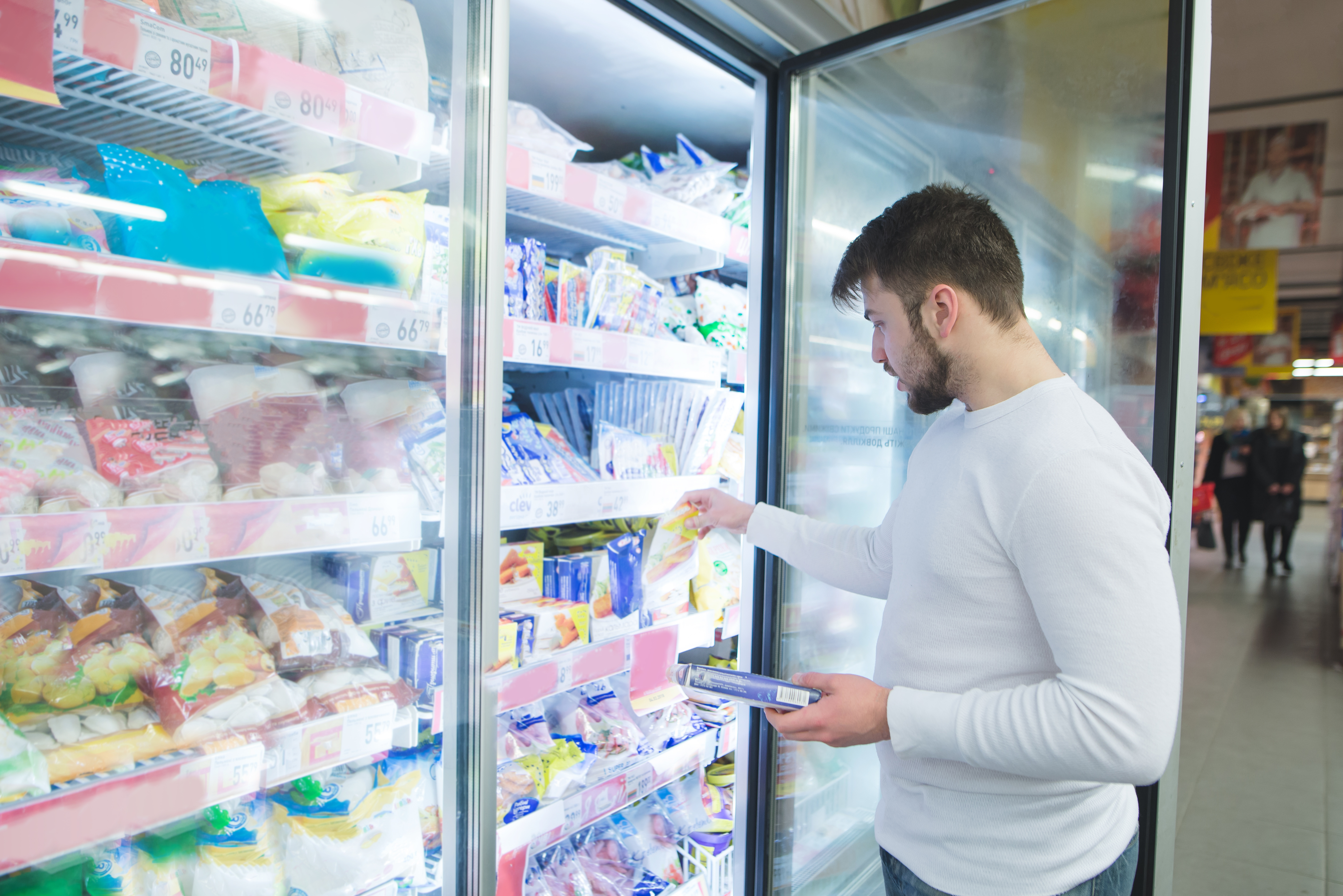 Man in white shirt pulling deli meat out of a supermarket freezer