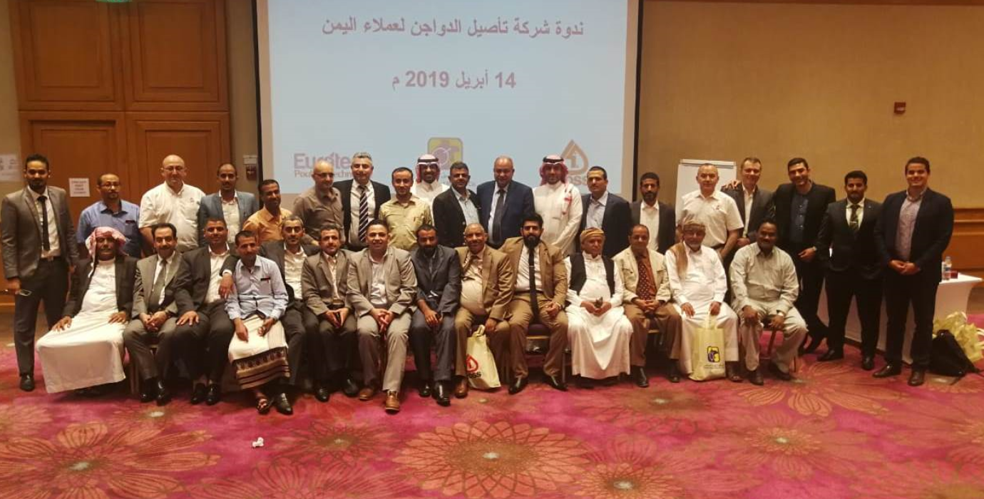 Group of 34 men pose in two rows in front of projection screen.