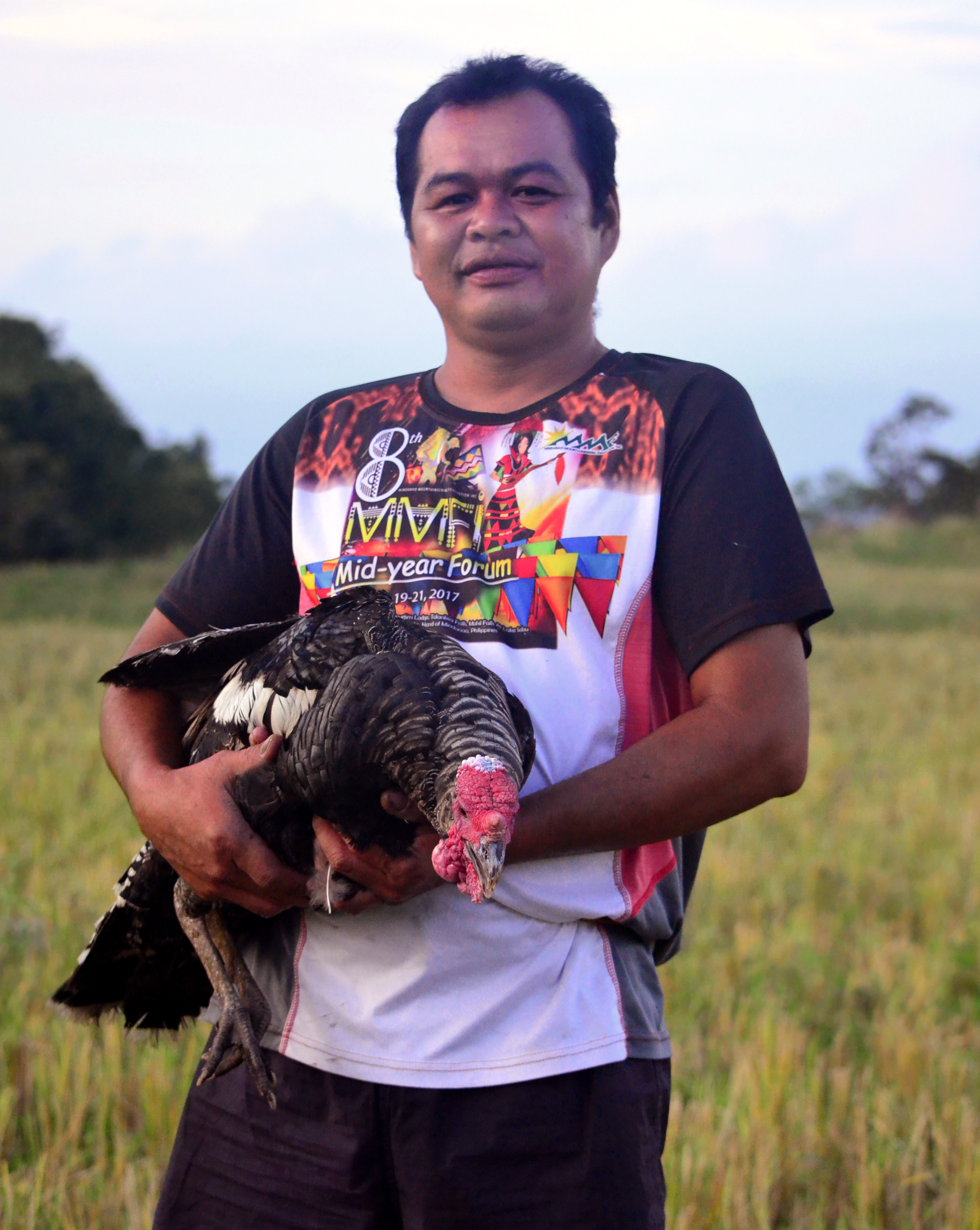 a man stands in a field and holds a turkey