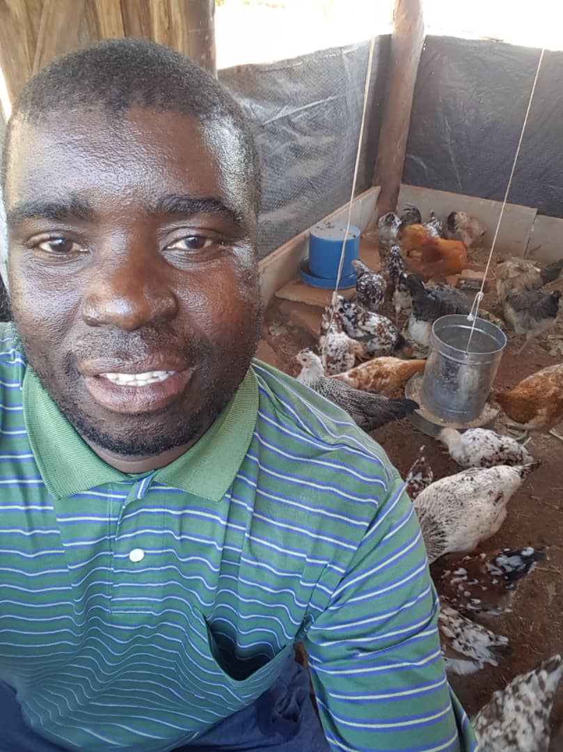 a man smiles at the camera with chickens in the background