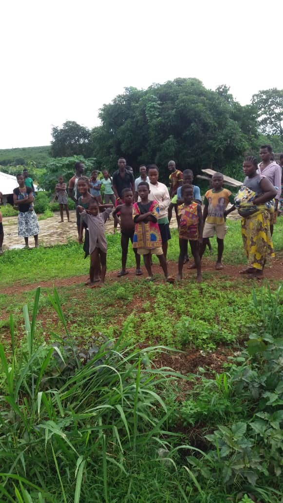 Children and community members in Sierra Leone stand at the grassy, undeveloped site