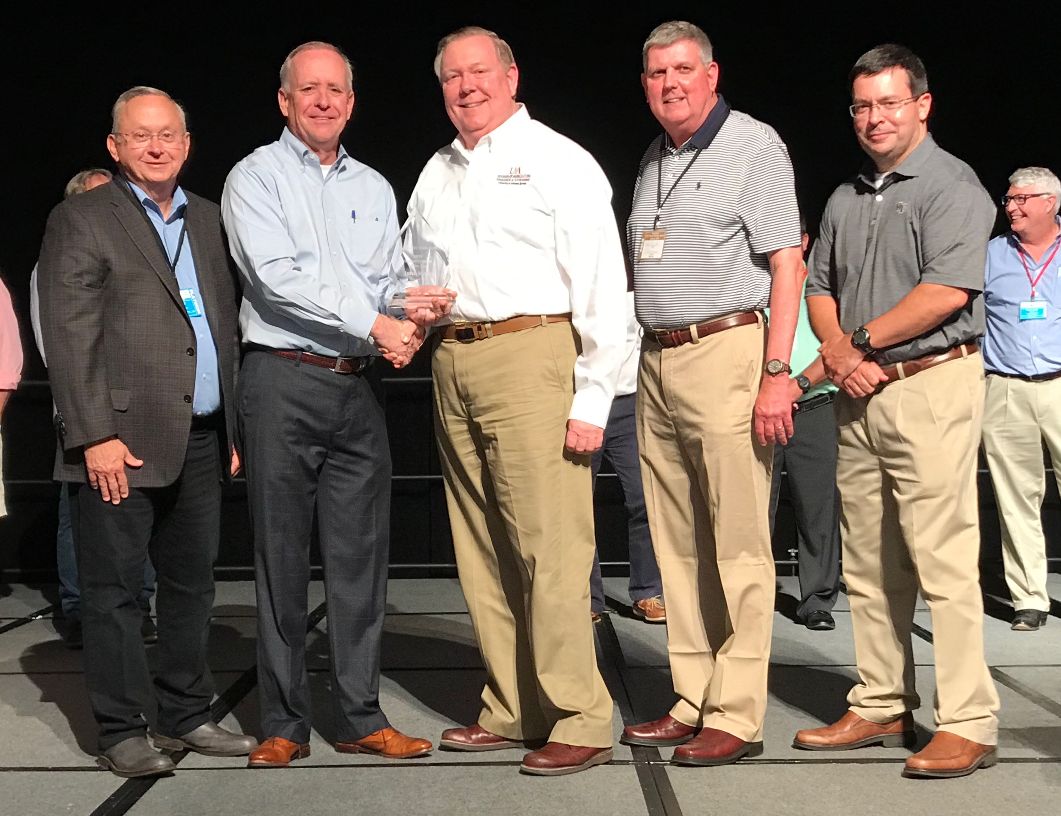 Marvin Childers, president of The Poultry Federation, shakes hands with John Marcy (white shirt), as Marcy was named the Industry Leader of the Year by TPF for 2019