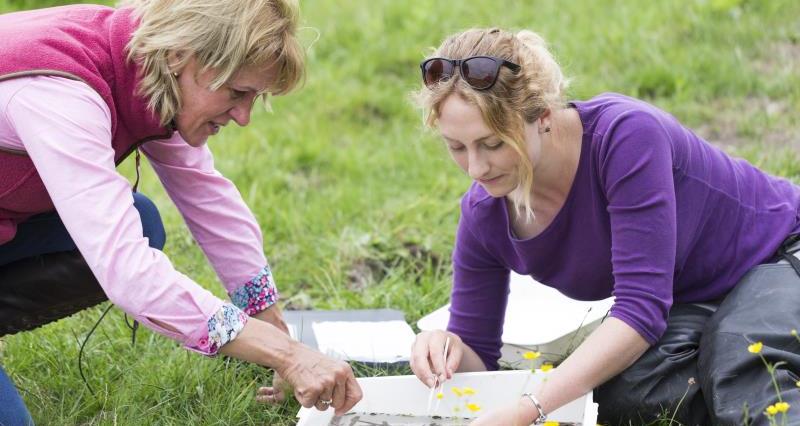 two women sit on the grass and write on paper