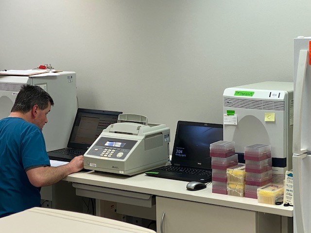 a man sits at a laptop with a machine next to it