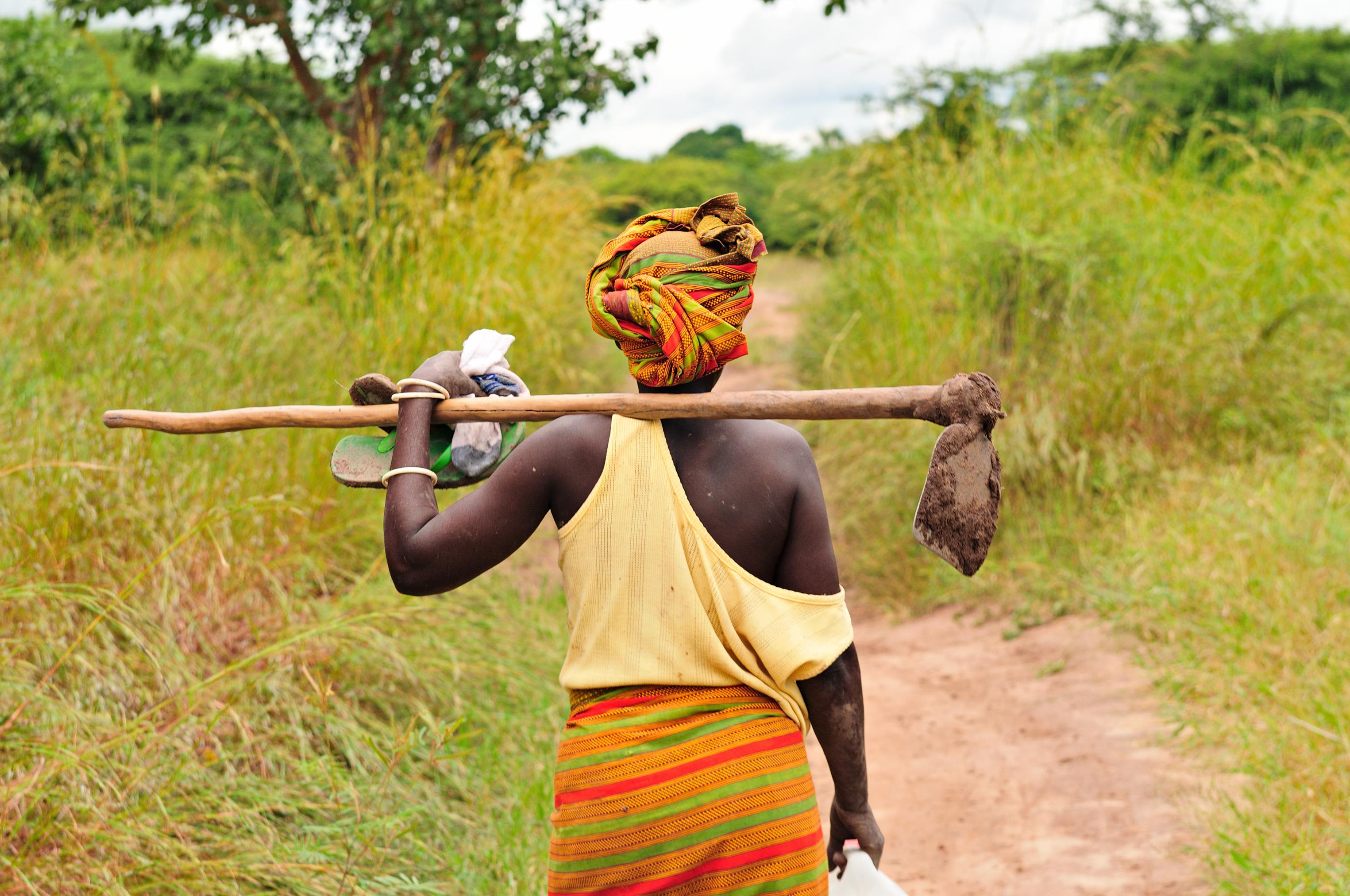 african woman carrying a tool on a grassy path
